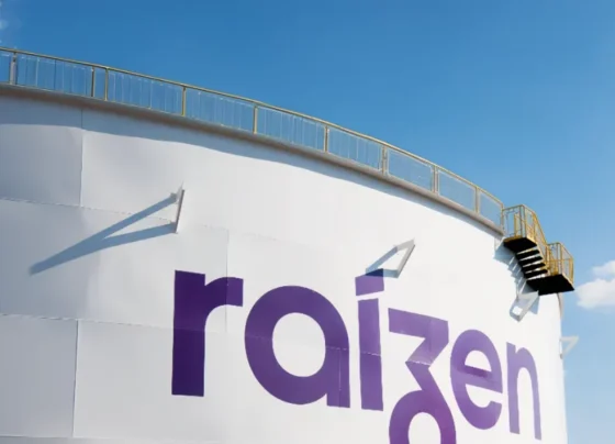 Tanque industrial branco com logotipo "raizen" em roxo, escada lateral e céu azul claro ao fundo.