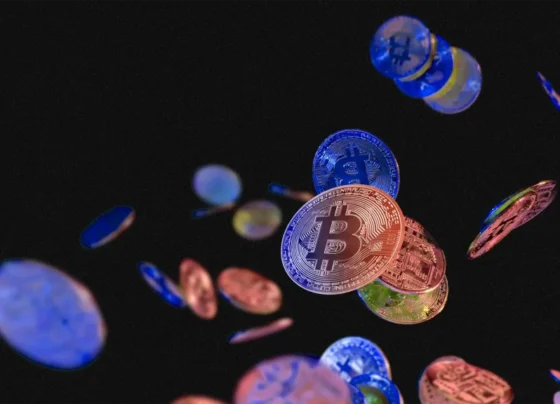 Moedas virtuais flutuam contra um fundo preto, com um Bitcoin destacado no centro, rodeado por tons metálicos de azul, vermelho e dourado.