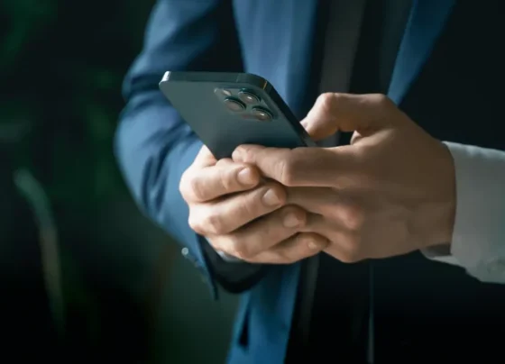 Em um ambiente interno suavemente iluminado, uma pessoa em um terno azul escuro segura um celular moderno com múltiplas lentes.