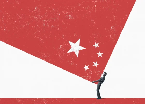 Figura humana em preto e branco segura uma superfície triangular branca contra um fundo vermelho com estrelas, remetendo à bandeira da China.